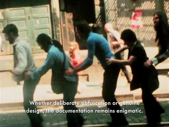 Film still of a street procession with a subtitle